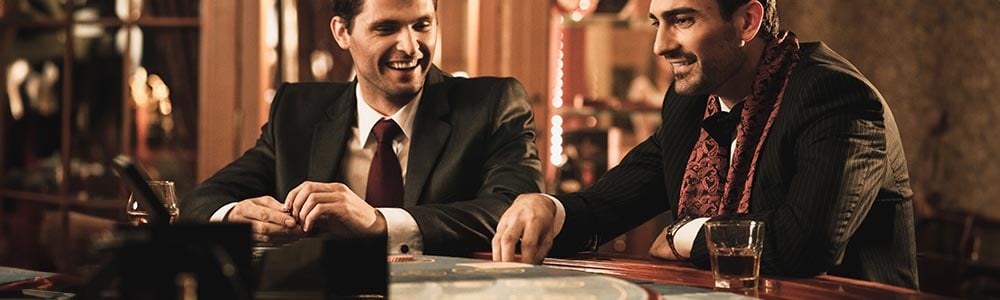 two men at a casino table with a drink