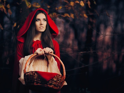 adult Little Red Riding Hood walking through the forest with a basket of apples