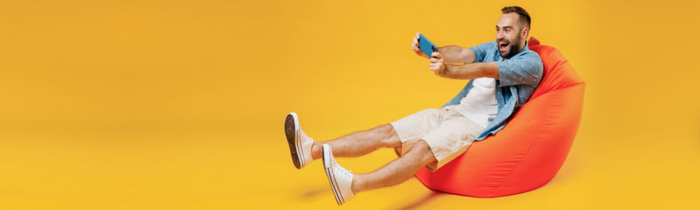 man sitting on a pillow chair celebrating a win on a game on a mobile device 