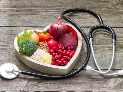 fruits, vegetables, grains and legumes in a heart shaped dish with a stethoscope around it