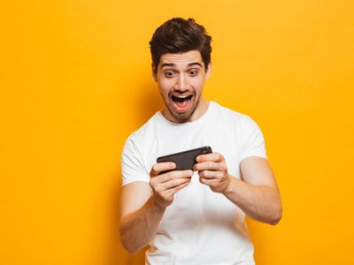excited young man playing on his smartphone with a yellow background