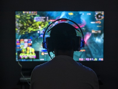 back of a gamer with headset on playing video game on a big screen