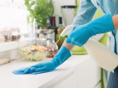 woman cleaning with blue gloves on and using cleaning spray on the counter top